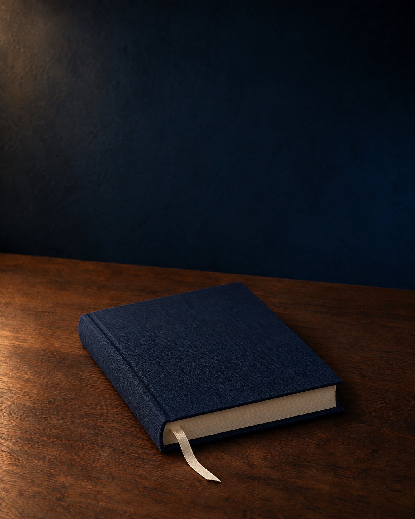 A midnight-blue clothbound book with a cream ribbon, on a walnut table