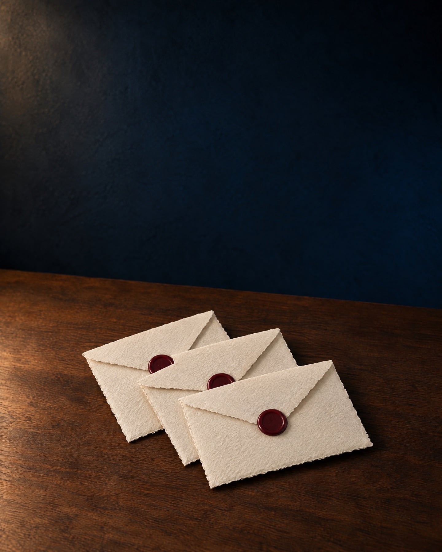 Three cream envelopes sealed with burgundy wax, fanned out on a walnut table